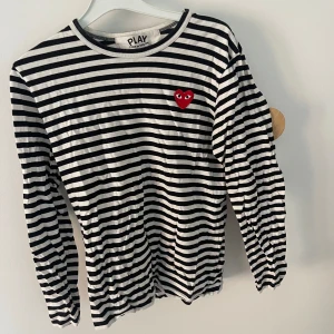 Randig långärmad tröja från Comme des Garçons - Säljer en superfin randig tröja från Comme des Garçons med deras ikoniska röda hjärta på bröstet. Den är svart och vit med långa ärmar, perfekt för både vardag och lite finare tillfällen. Tröjan är i bra skick och passar perfekt till jeans eller kjol!