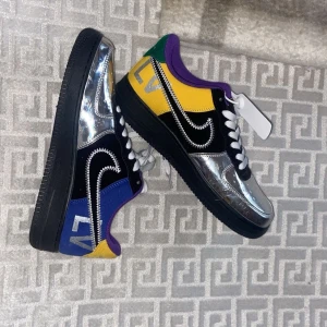 Färgglada sneakers med metallic detaljer - Säljer ett par unika sneakers i samarbete mellan Nike och Louis Vuitton. Skorna har en cool mix av färger som blå, gul, grön och lila med en metallic silver finish på ovandelen. De har en svart sula och klassisk snörning. Perfekta för att sticka ut i mängden!