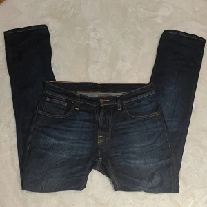 Nudie Jeans grim Tim  - Säljer ett par snygga mörkblå jeans från Nudie Jeans i modellen grim Tim. Jeansen är i storlek 30/32. 