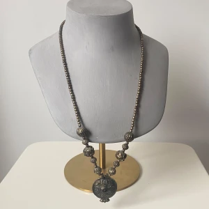 Antikt halsband med stora pärlor - Säljer ett unikt rustikt halsband med stora, detaljerade pärlor i en mörk silverfärg. Halsbandet har en stor rund medaljong som hänge, vilket ger det en vintage och elegant känsla. Perfekt för att ge en klassisk touch till din outfit!