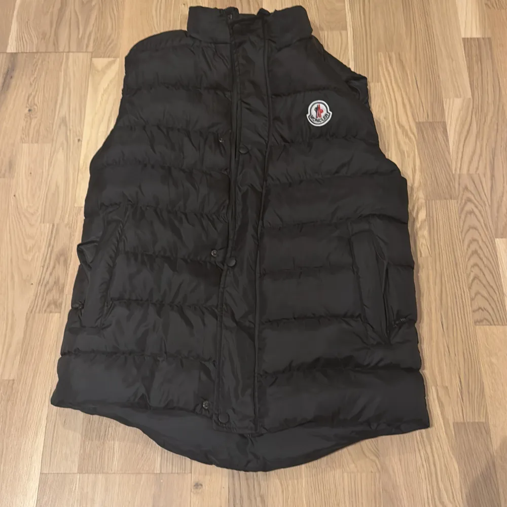 Säljer en snygg och varm svart dunväst från Moncler. Västen har en quiltad design med en dragkedja och knappar framtill. Perfekt för hösten som kommer nu. Har använt den kanske 2 gånger. Jackor.