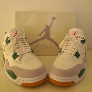 Nike Air Jordans i vitt och grönt - Säljer ett par snygga Nike Air Jordans i vitt och grönt. Skorna har en klassisk design med gröna detaljer och en röd Jumpman-logga på plösen. De är i nyskick och har en cool kombination av skinn och syntetmaterial.