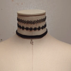 Svarta chokerhalsband i olika stilar - Säljer ett set med tre svarta chokerhalsband. Det första är ett elastiskt, snirkligt mönster som ger en cool 90-talsvibe. Det andra har små blommor som ger en söt och edgy look. Det tredje är ett enkelt svart band med en liten triangelformad hängande detalj. Perfekt för att ge din outfit en extra touch!