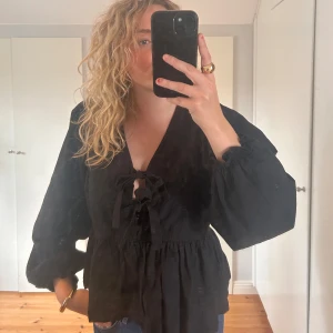 Svart blus från Neo Noir - Säljer en svart blus från Neo Noir. Den har långa ärmar och en v-ringad design med knytning framtill. Perfekt för både vardag och festliga tillfällen. Blusen är i ett mjukt och bekvämt material.🖤🍸🪩🍂🎀