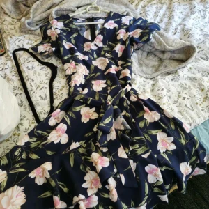 Blommig klänning från Shein - Säljer en helt ny superfin blommig klänning från Shein. Den är marinblå med stora rosa och vita blommor. Klänningen har en omlott-design med en v-ringad hals och korta ärmar. Perfekt för sommarens fester eller en dag på stan!