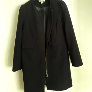Svart kappa H&M  - Svart kappa från H&M. Fint skick då den knappt är använd pga fel storlek. Mellanlång, gullig dragkedja, diskret "puff"detalj vid axeln (se bild).  - Storlek 40 (liten i storleken, så passar mer en 36-38)