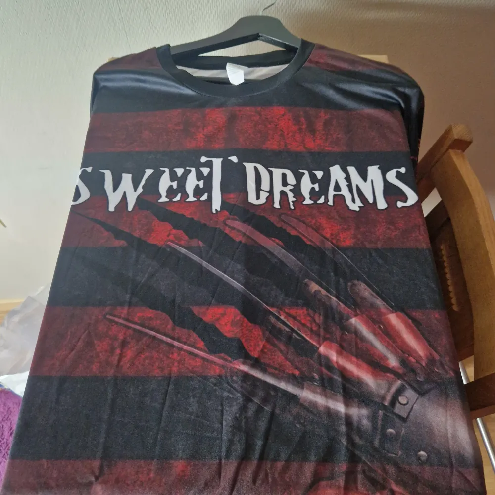 En svart och röd t-shirt med tryck av Freddy Krueger från Nightmare on Elm Street. På framsidan syns Freddy's hand med klor och texten 