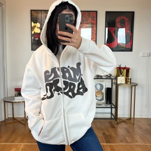 Vit hoodie med tryck 💞 - Säljer en superbekväm vit hoodie med coolt svart tryck på framsidan. Den har en dragkedja och en stor huva som gör den perfekt för kyliga dagar. Hoodien har en avslappnad passform och är gjord i mjukt material. Perfekt för både vardag och chill!