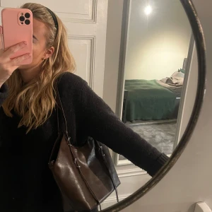 Brun axelväska i skinn - Snygg brun axelväska i skinn med långa remmar. Perfekt för att bära med sig allt man behöver. Väskan har en stilren design med dekorativa remdetaljer på sidorna. Inga defekter! Perfekt skol eller jobbväska!!! 