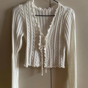Vit och svart ribbad kofta - Säljer två ribbade koftor i vitt och svart. Båda har långa ärmar och en v-ringad design med knytning framtill. De är croppade med volangdetaljer längs kanterna. Perfekta för lager-på-lager-stil! 120kr för båda! 