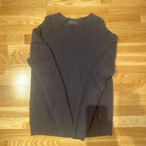 Svart stickad tröja från Religion - Säljer en svart stickad tröja från Religion med ett diskret mönster och broderad detalj. Tröjan har långa ärmar och en rund halsringning. Perfekt för kyligare dagar.