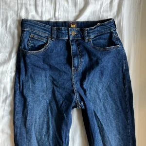 Blå jeans från Lee - Snygga blå jeans från Lee med klassisk femficksdesign och knappgylf. Perfekta för en avslappnad stil. Märkeslogga på baksidan ger en autentisk touch.