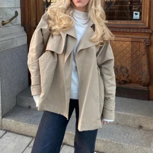 Beige trenchcoat  - Snygg beige trenchcoat med klassisk krage och långa ärmar. Jackan har en lös passform och stilrena detaljer som gör den perfekt för höst och vår. Ett måste i garderoben för en chic look!
