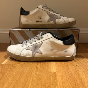 Golden goose  - Snygga vita sneakers med en grå stjärna på sidan och svarta detaljer vid hälen. Skorna har en klassisk snörning och en bekväm sula i gummi. Perfekta för en avslappnad stil.