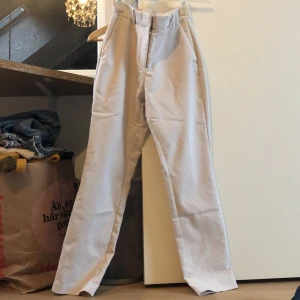 Beige kostymbyxor från H&M - Snygga beige/vita kostymbyxor från H&M med hög midja och raka ben. Byxorna har diskreta bakfickor och en stilren design som passar perfekt för en chic look. Perfekta för att ge en elegant touch till din outfit.