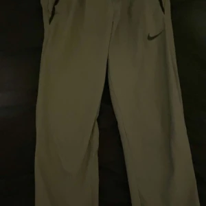 Gråa byxor från Nike - Snygga gråa  byxor från Nike med en avslappnad passform. Perfekta för en casual look. Byxorna har fickor och en diskret Nike-logga på sidan. Vid snabb affär pris säkning 