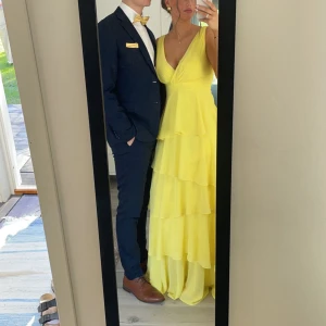 Balklänning  - Gul långklänning med volanger och v-ringad. Använd en gång på bal förra året. Klänningen uppfattas olikt gul beroende på ljus. Jag är 171 cm och hade även klack med 5cm extra men klänningen var fortfarande ned till backen. 