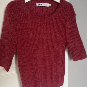 Röd ribbad tröja från ONLY - Säljer en snygg röd ribbad tröja från ONLY i storlek XS. Tröjan har trekvartsärmar och en rund halsringning, perfekt för både höst och vår. Ett stilrent plagg som passar till många olika outfits.