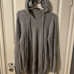 Grå stickad hoodie - Mysig grå hoodie. Perfekt för kyliga dagar med sin mjuka och bekväma passform. Den har en justerbar huva med snören och ribbade muddar vid ärmslut och nederkant. Ens silver saken saknas i slötet av snören (bild 3)annars inga skador! 