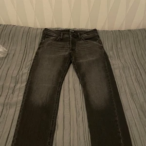 Svarta Jeans - Snygga svarta jeans från Jack and Jones med klassisk femficksdesign och knappgylf. Perfekta för en stilren look. Passar bra till både vardag och mer uppklädda tillfällen. Storlek 30/32 osäker på modell. Nypris kring 1k aldrig använda