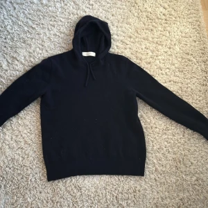 Mörkblå kashmir hoodie från Sayless - Säljer en stilren mörkblå hoodie i mjuk kashmir från Sayless. Perfekt för kyliga dagar med sin bekväma passform och klassiska design. Huvan ger extra värme och stil. Ett måste i garderoben för den som älskar komfort och kvalitet. Den har en design med snören som är riktigt snygg. Jag säljer då den är för liten. Skicket är 8/10 bara använd ett fåtal gånger, inga defekter.