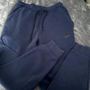 Mörkblå mjukisbyxor från Nike - Säljer ett par mörkblå mjukisbyxor från Nike med snörning i midjan och sidofickor. Perfekta för en avslappnad stil. Nike-loggan är diskret placerad på benet. En av den skönaste byxorna sitter perfekt jag har för många Nike techs så tänkte sälja den 