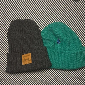 Två stickade mössor i grått och grönt - Två snygga stickade mössor, en i grått med en läderlapp från Appetiff och en i grönt med en broderad logga.