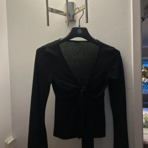 Svart långärmad topp från Gina Tricot!! - Snygg svart långärmad topp från Gina Tricot i storlek XS. Toppen har en knytning framtill. Säljer då den inte kommer till användning! 