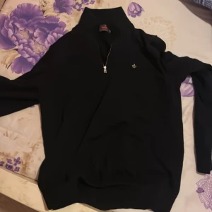 Svart tröja med dragkedja från Morris - Snygg svart tröja från Moris med halv dragkedja och en liten logotyp på bröstet. Perfekt för en stilren look. Tröjan har långa ärmar och en hög krage. Oanvänd. Nypris 1500