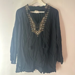 Blus Ralph Lauren  - Snygg och elegant blus från Denim & Supply Ralph Lauren.  Blusen är svart med vackra guld- och silverfärgade broderier runt halsringningen och på axlarna. Broderiet är i fint skick men kan ha några lösa trådar, se bild 5. Den har en v-ringad hals med band att knyta. Blusen är i en mjuk och skön kvalitet. Storlek M
