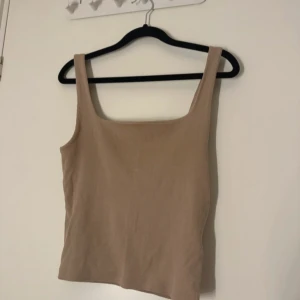 Beige ribbad linnetopp från Bik Bok - Säljer en stilren beige ribbad linnetopp från Bik Bok. Perfekt för varma dagar med sin ärmlösa design och bekväma passform. Ett måste i garderoben för en enkel och snygg look. 