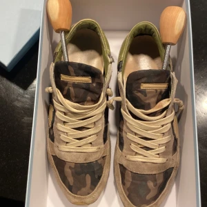 Camouflage sneakers från Philippe Model - Snygga sneakers från Philippe Model med ett coolt camouflage-mönster. Skorna har beige snörning och detaljer i mocka. Perfekta för en avslappnad stil med en touch av edge. Jag är öppen för byten 