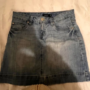 Jeanskjol från Lindex - Snygg jeanskjol från Lindex i klassisk blå denim. Kjolen har en kort längd och femficksdesign med knapp och dragkedja framtill. Perfekt för en avslappnad stil.