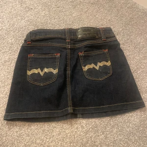 Mörkblå jeanskjol med broderade detaljer - Trendig mörkblå jeanskjol med snygga detaljer på bakfickorna. 