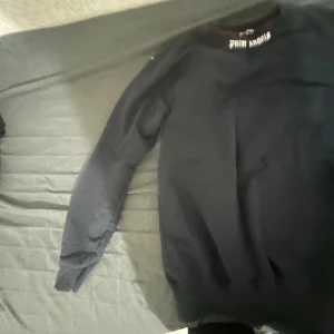 Svart tröja från Palm Angels - Säljer en svart tröja från Palm Angels med deras ikoniska logga i vitt på framsidan. Tröjan har långa ärmar och en rund halsringning. Perfekt för en stilren och avslappnad look.