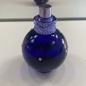 Blå parfymflaska med strassdetaljer - Elegant blå parfymflaska i rund form med glittrande strassdetaljer. Flaskan har en silverfärgad spraytopp och ett dekorativt mönster runt halsen. Perfekt för den som älskar en lyxig och iögonfallande design.
