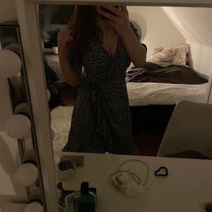 Blommig klänning med knyt - Säljer en söt blommig klänning med v-ringning och knyt i midjan. Klänningen har korta ärmar och ett fint mönster i vitt och mörkblått. Perfekt för en somrig look!💞