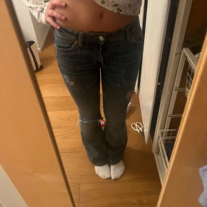 Blå jeans med slitningar - Säljer ett par blå jeans med slitningar och hål som jag klippt själv. Lågmidjade och bootcut, upplagda med innerbenslängden 75 och midjemått 34.