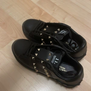 Svarta Valentino skor - Snygga svarta sneakers med guldfärgade nitar. De är i storlek 37 men själv har jag 38 och de passar mig. Har inte använd jätte många gånger och de är i ett fint skick. Får inte användning av de och vill få de sålda därav priset men pris kan diskuteras