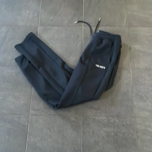 Svarta mjukisbyxor från Les Deux - SÖKER BRA PRIS!! Snygga svarta mjukisbyxor från Les Deux med snörning i midjan och en stilren design. Perfekta för en avslappnad look. Byxorna har en broderad logga på sidan och är gjorda i ett mjukt material. Ny pris är 1000kr+