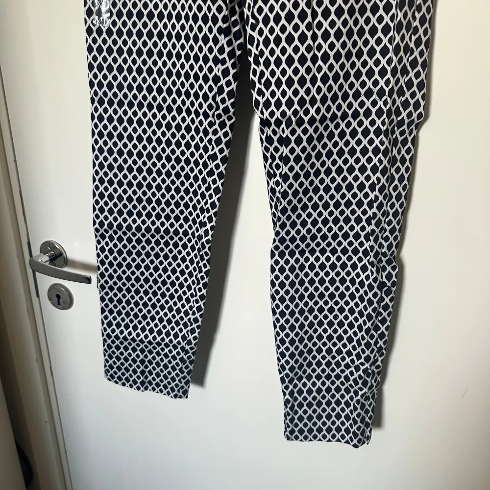 Snygga svartvita byxor med ett unikt mönster. De har en rak passform och är perfekta för att ge en stilren look. Byxorna är tillverkade i ett bekvämt material som passar bra för olika tillfällen. Storlek XS. Helt ny med tags. . Farkut & Housut.