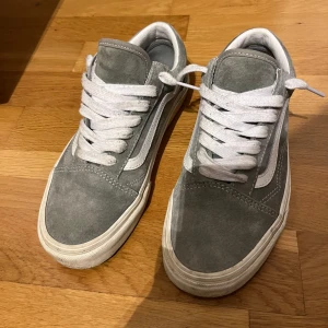Grå sneakers från Vans - Säljer ett par grå sneakers från Vans med vit sula och klassisk vit sidostrimma. Skorna har snörning och är tillverkade i mocka, men är impregnerade. Knappt använda någon gång så därför säljer jag de. Passar 38/39. OBS, Priset kan gå ner vid snabb affär. Nypris ca 1000kr