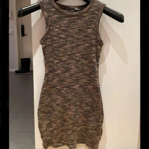 Mönstrad ärmlös klänning från H&M Divided - Säljer en cool ärmlös klänning från H&M Divided i ett mönstrat tyg med jordnära toner. Klänningen är ribbad och har en tight passform som framhäver figuren. Perfekt för en avslappnad stil eller att klä upp med accessoarer.