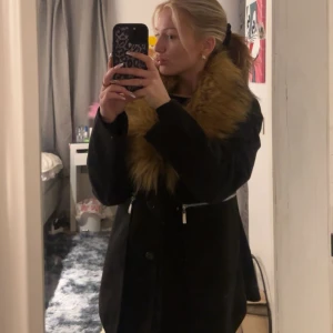 Svart kappa med fuskpäls - Säljer en elegant svart kappa med stor krage i fuskpäls. Jackan har dragkedja och knappar framtill samt långa ärmar. Kappan är från DM😆