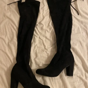 Svarta overknee boots - Snygga svarta overknee boots med hög klack och snörning upptill. Perfekta för att ge en stilren look till din outfit. Tillverkade i mocka för en lyxig känsla.