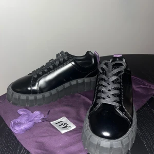 Svarta Odessa Eytys - Snygga svarta sneakers från Eytys med en chunky sula och glansig finish. Skorna har svarta snören och en lila flik baktill för en extra touch. Perfekta för en stilren look. Det tillkommer extra skosnöre i lila. Jag har samma i vit så vet att de är otroligt sköna. Använda endast en gång. 
