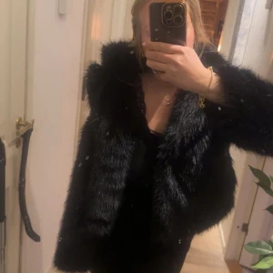 Svart pälsjacka - Säljer en elegant svart pälsjacka med fluffig textur. Jackan har en klassisk design och är perfekt för att hålla dig varm och stilren under kyliga dagar. Den är lätt att matcha med olika outfits och ger en lyxig känsla.