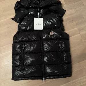 Svart väst från Moncler - Säljer denna västen från moncler. Luvan går ta bort. Den är aldrig använd ute. Jag har fått den i present så är INTE säker på äktigheten så du köper på din egna risk. Västen har ett jätte litet hål som knappt går att se därför säljer jag så billigt. Kontakta om du har några funderingar!