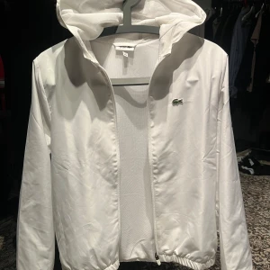 Vit vindjacka från Lacoste - Tjena säljer min vita vindjacka från Lacoste använd 2 gånger pågrund av att den verkligen är för liten, skick 10-10 storlek 164 cm  köpte för 1300 kr, mitt pris 1000 kr pris kan diskuteras är du intresserad så är de bara höra av sig🙌🏼 