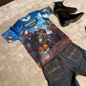 Blå Fortnite t-shirt - Cool blå t-shirt med Fortnite-tema och tryck av karaktärer i Halloween-stil. Perfekt för fans av spelet som vill visa sin passion. Kortärmad och tillverkad i ett bekvämt material.